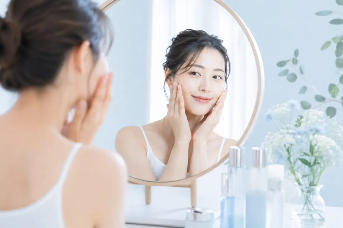 鏡に映る自分の笑顔を見つめ、嬉しそうに肌をケアする女性